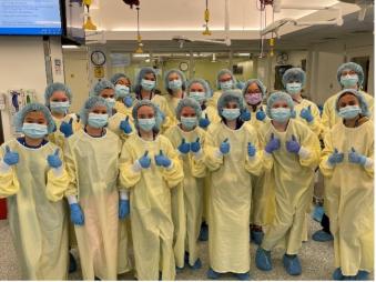 a group of middle school children dressed in full surgical gear giving thumbs up to camera.